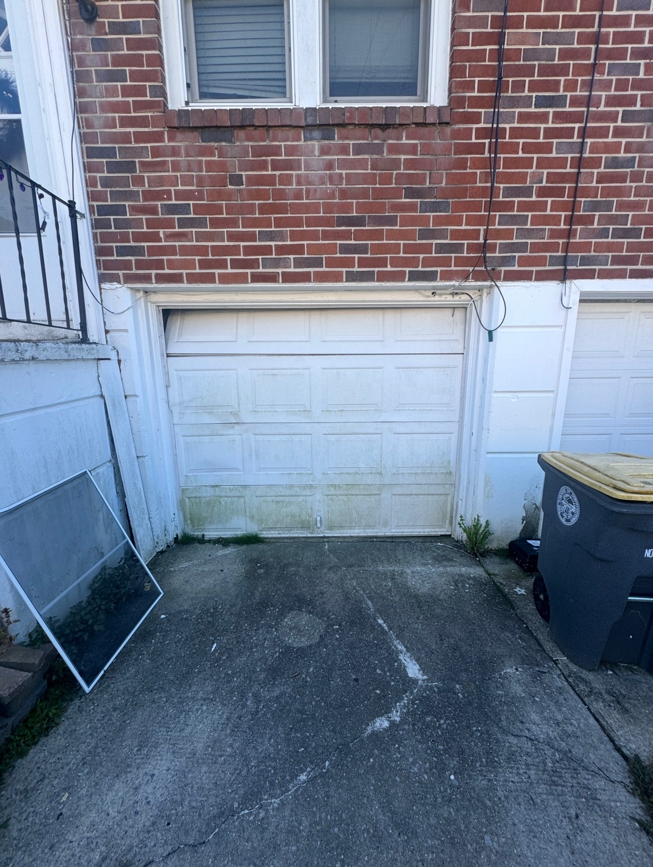 Before: Old worn garage door with green staining and damage on brick townhouse